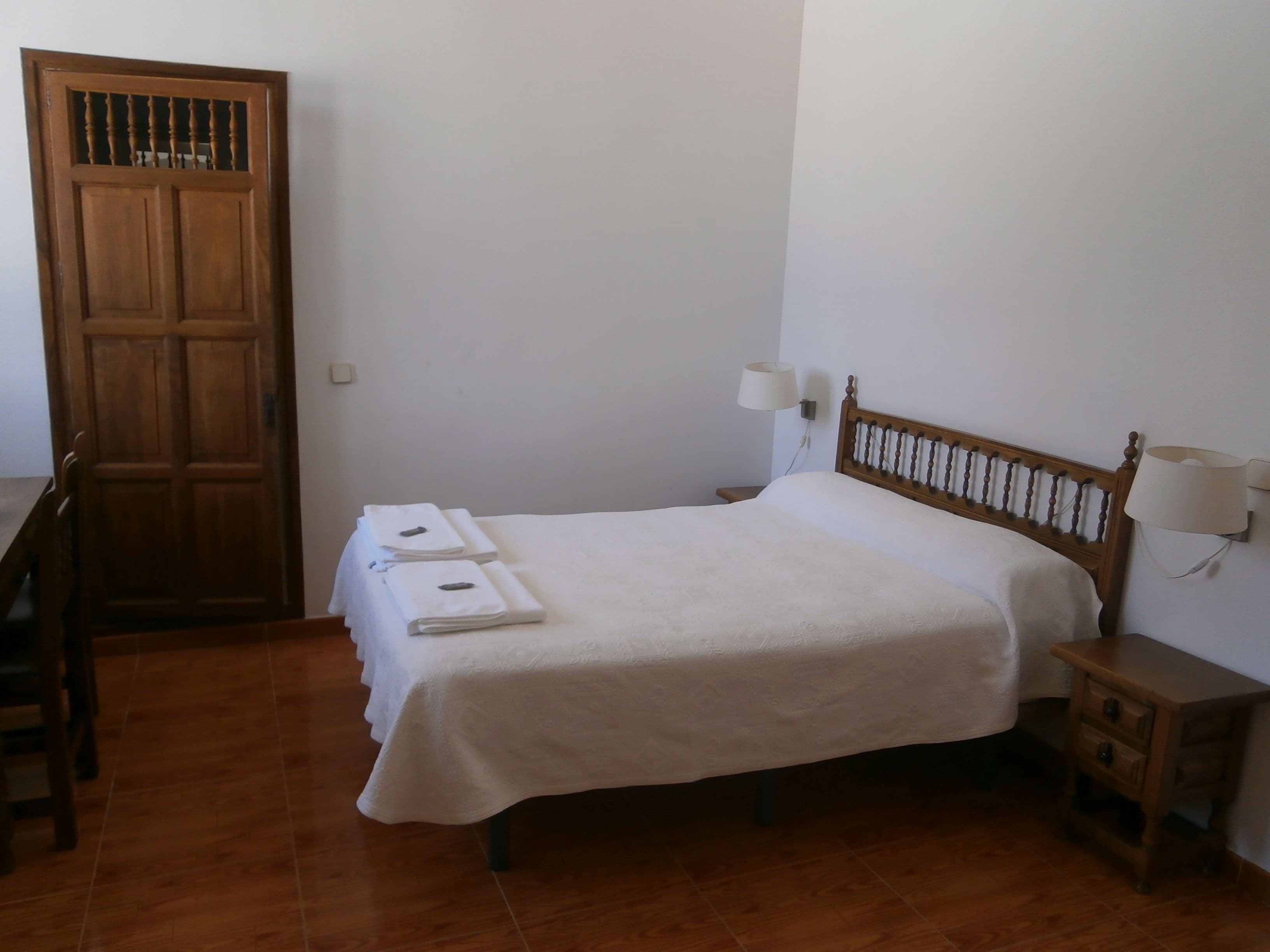 A simple room with a bed, a wooden door, a nightstand, and a chair.