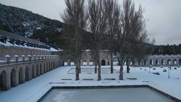 Un patio con suelo cubierto de nieve, una piscina y un edificio con ventanas arqueadas y un balcón.