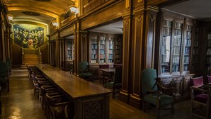 Ein langer Holztisch mit Stühlen, umgeben von Bücherregalen und einer Treppe, die in eine obere Ebene führt.