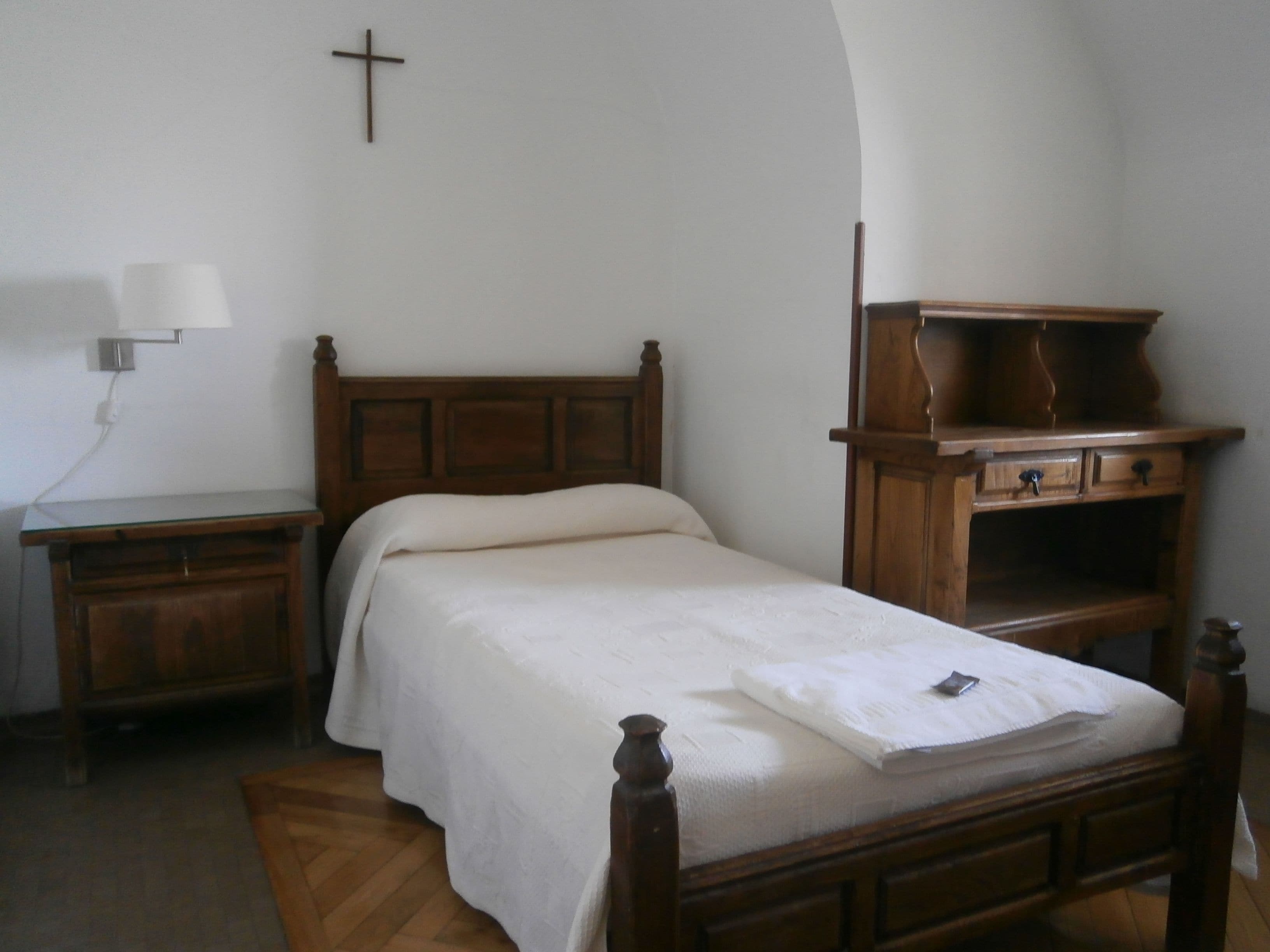 A bedroom with a wooden bed, a nightstand, a dresser, and a cross on the wall.