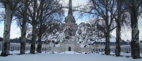 A snow-covered landscape with a prominent cross monument surrounded by trees.