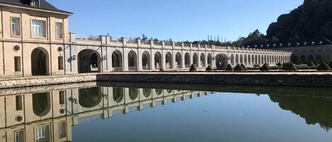 A long, arched bridge over a calm body of water, reflecting the structure and surrounding greenery.