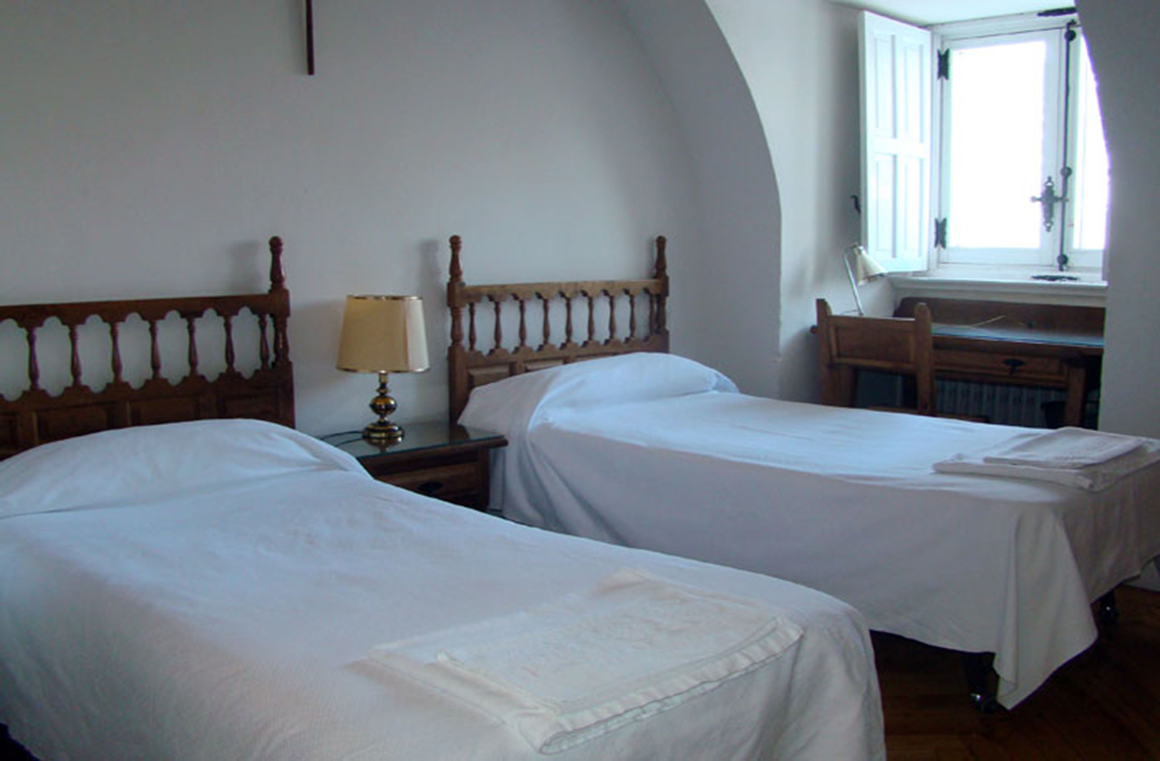 Une chambre avec deux lits, une table de chevet avec une lampe, une commode en bois et une fenêtre avec des rideaux.