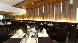 Un restaurante con mesas y sillas de madera oscura, servilletas blancas y cristalería.