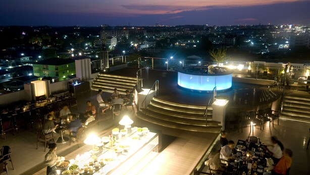 Un restaurante en la azotea con mesas al aire libre, escenario y vistas a la ciudad al anochecer.