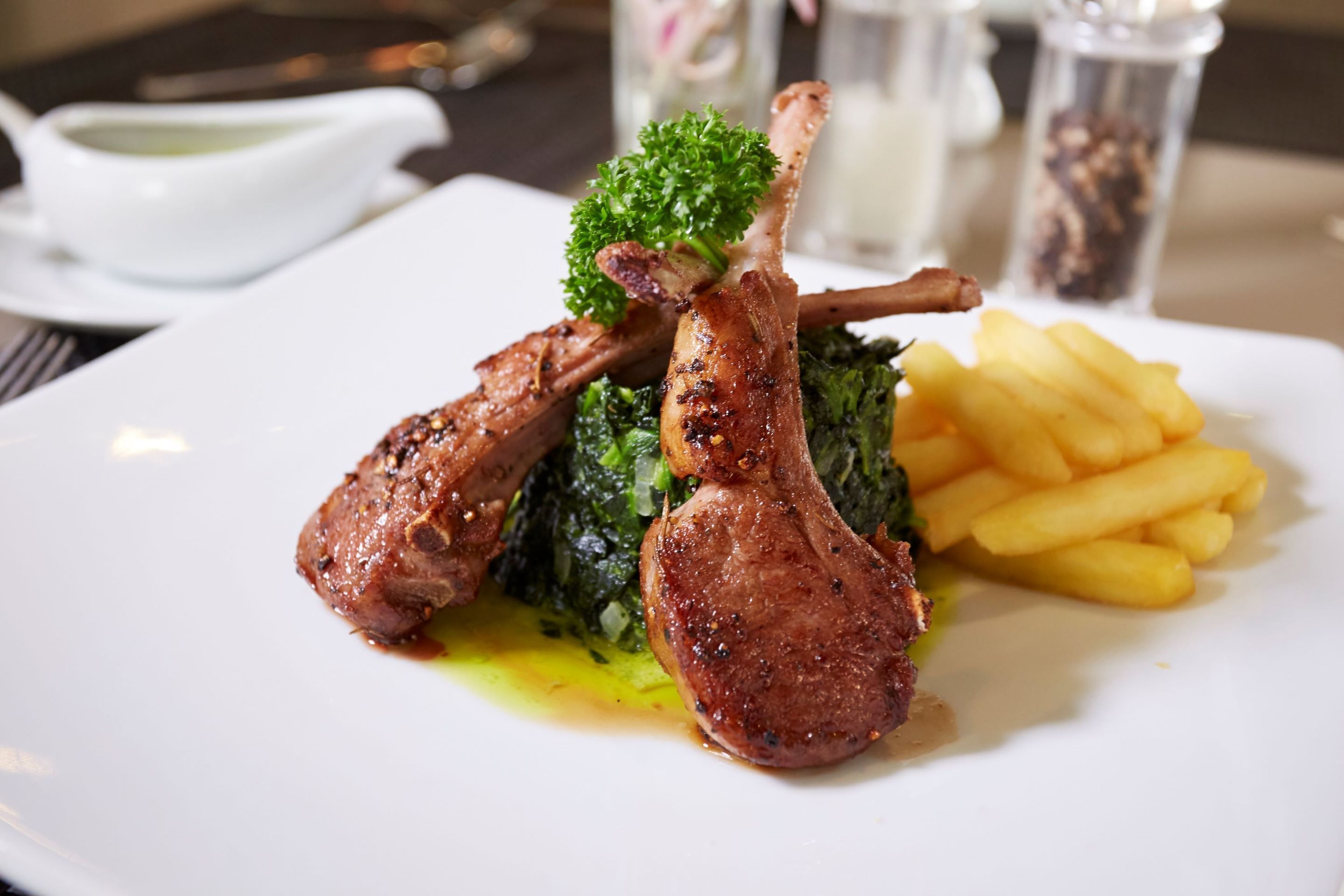 A plate with grilled lamb chops, greens, and fries.