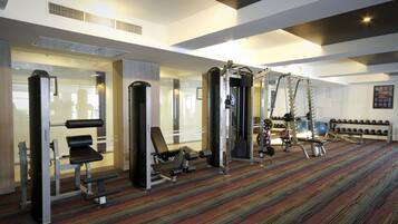 A gym with various exercise equipment, including weight machines and free weights, arranged in a spacious room with a patterned carpet.