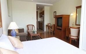 A hotel room with a bed, a desk, a chair, a television, and a kitchenette in the background. - Kameo Grand Rayong Hotel & Serviced Apartments (Rayong)