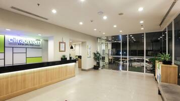 A modern reception area with a wooden reception desk, a sign for 'CitraDream', and a glass door leading to a balcony with outdoor seating.
