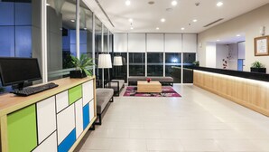 A modern reception area with a wooden reception desk, a seating area with a sofa and a coffee table, and large windows providing a view of the outside. - Hotel Citradream Semarang (Semarang)