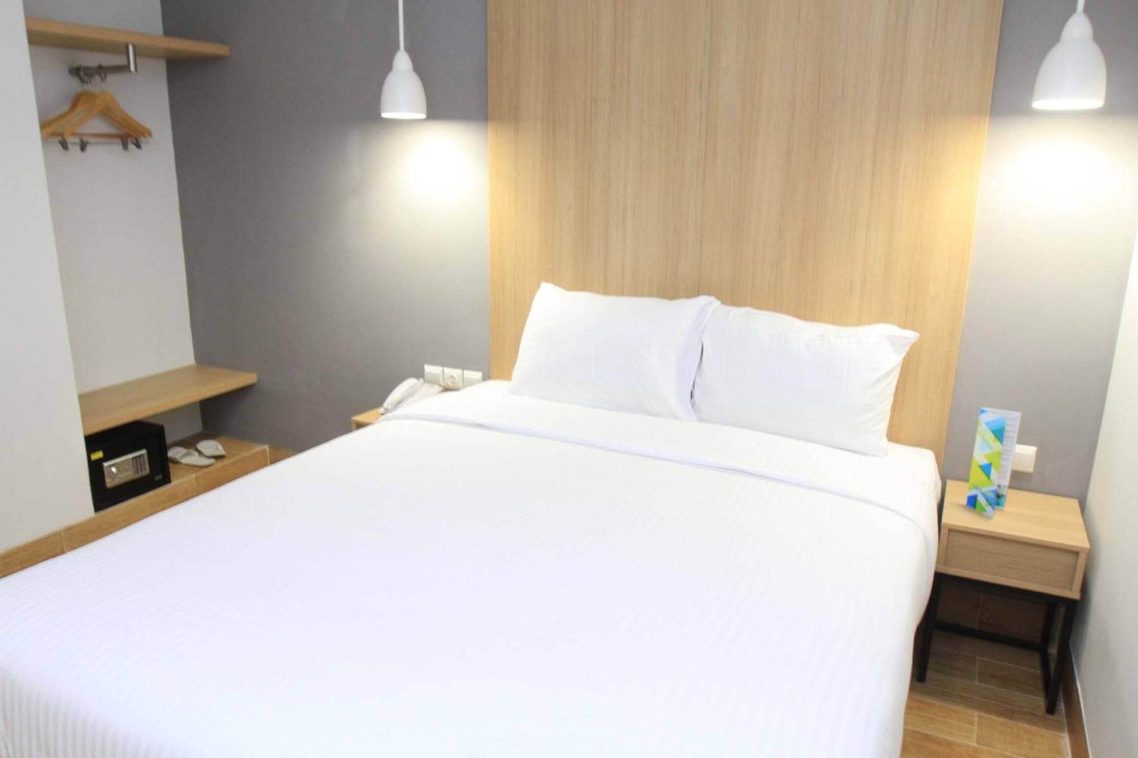 Een net opgemaakt bed met witte lakens, een houten hoofdbord en twee nachtkastjes met lampen.