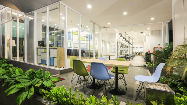 Un espacio interior moderno con separaciones de vidrio, una mesa larga con sillas y plantas de interior.