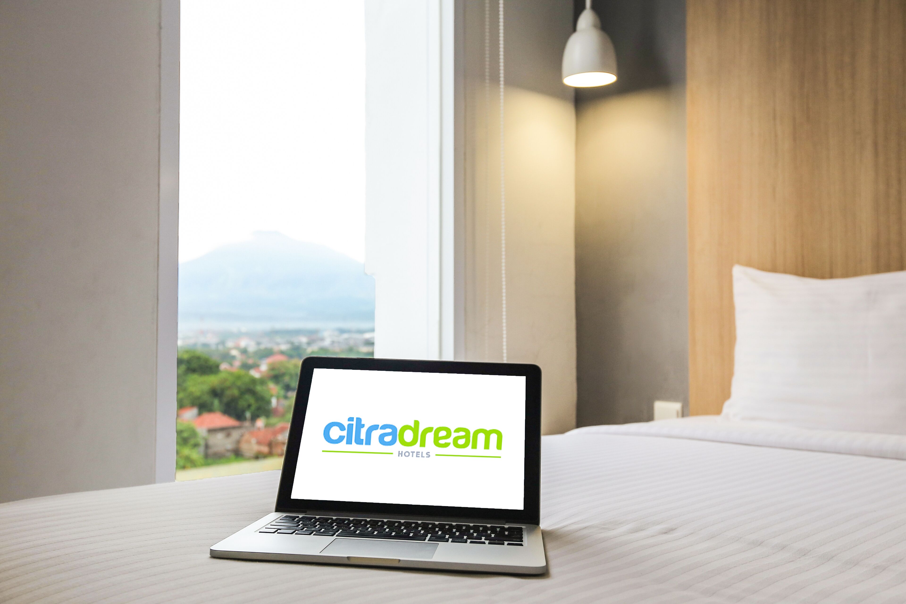 A laptop on a bed displaying 'citradream hotels' with a cityscape view through a window.