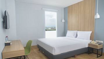 A hotel room with a bed, a desk, a chair, a TV, a window with a view, and a bedside table with a phone and lamp.