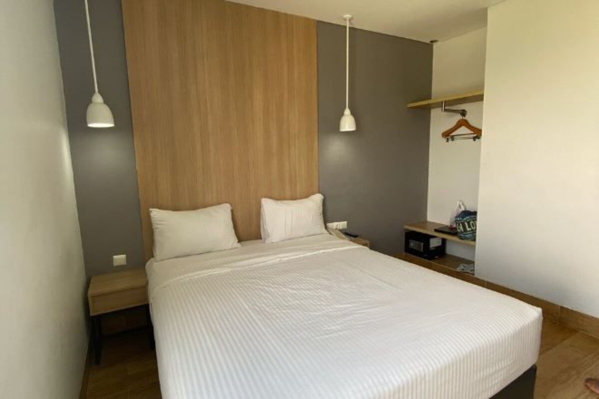 Une chambre moderne avec un grand lit, une tête de lit en bois, deux tables de chevet et un luminaire suspendu.