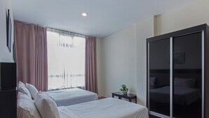 Habitación de hotel con dos camas, armario con puerta corredera, una mesita con una planta y un ventanal grande con cortinas.