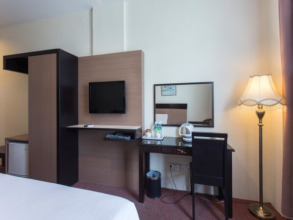 Et hotelværelse med en seng, et skrivebord med et fladskærms-tv, et spejl, en lampe og en skraldespand.