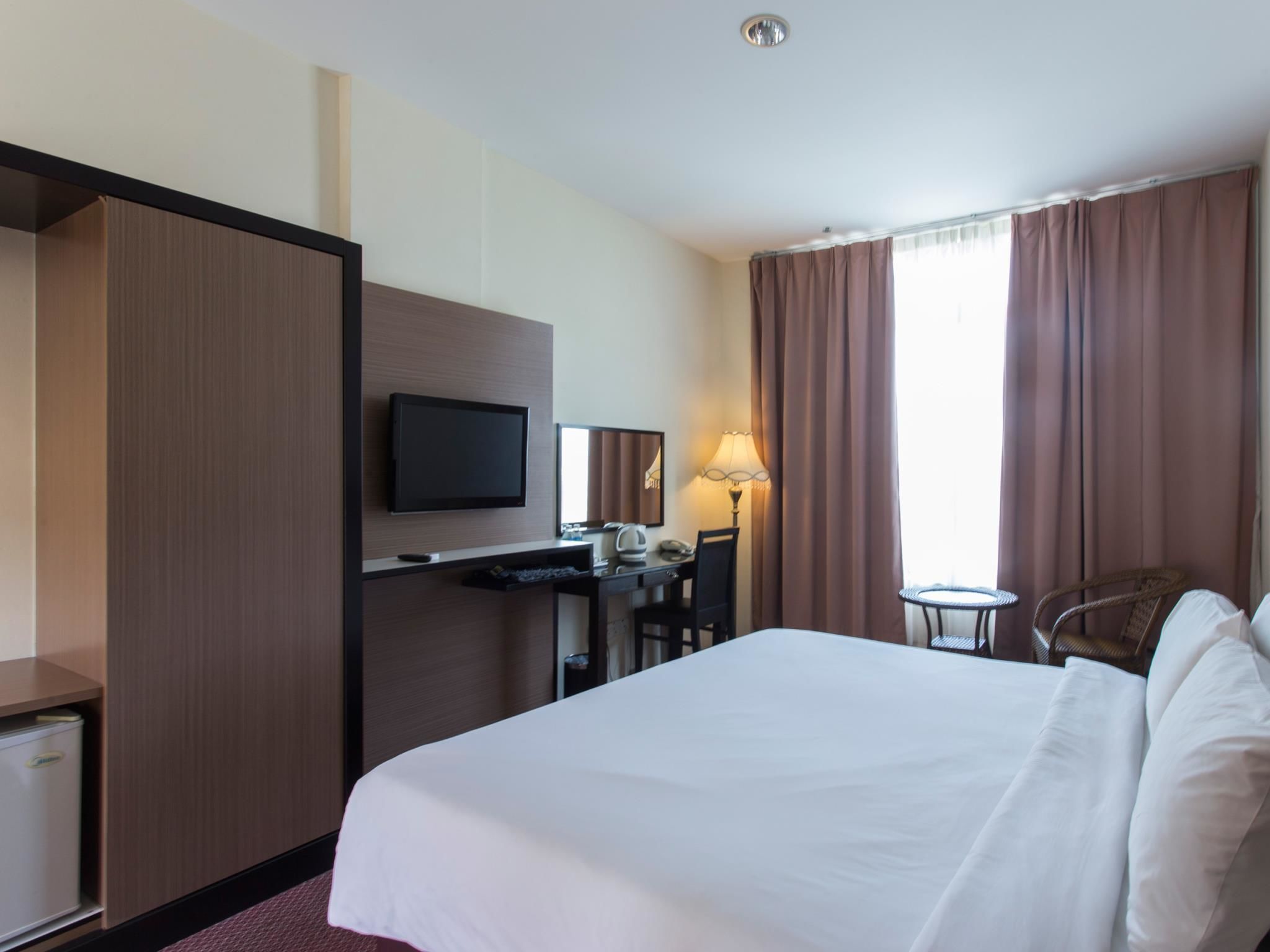 A hotel room with a bed, a desk with a computer, a television, and a chair.