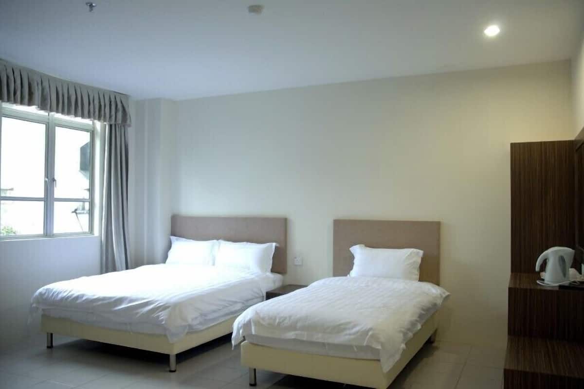 Quarto de hotel com duas camas de solteiro, uma janela com cortinas, um guarda-roupa de madeira e uma pequena mesa com chaleira.