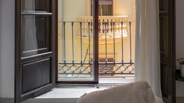 Una habitación de hotel con un gran ventanal corredera que da a un balcón con barandilla.