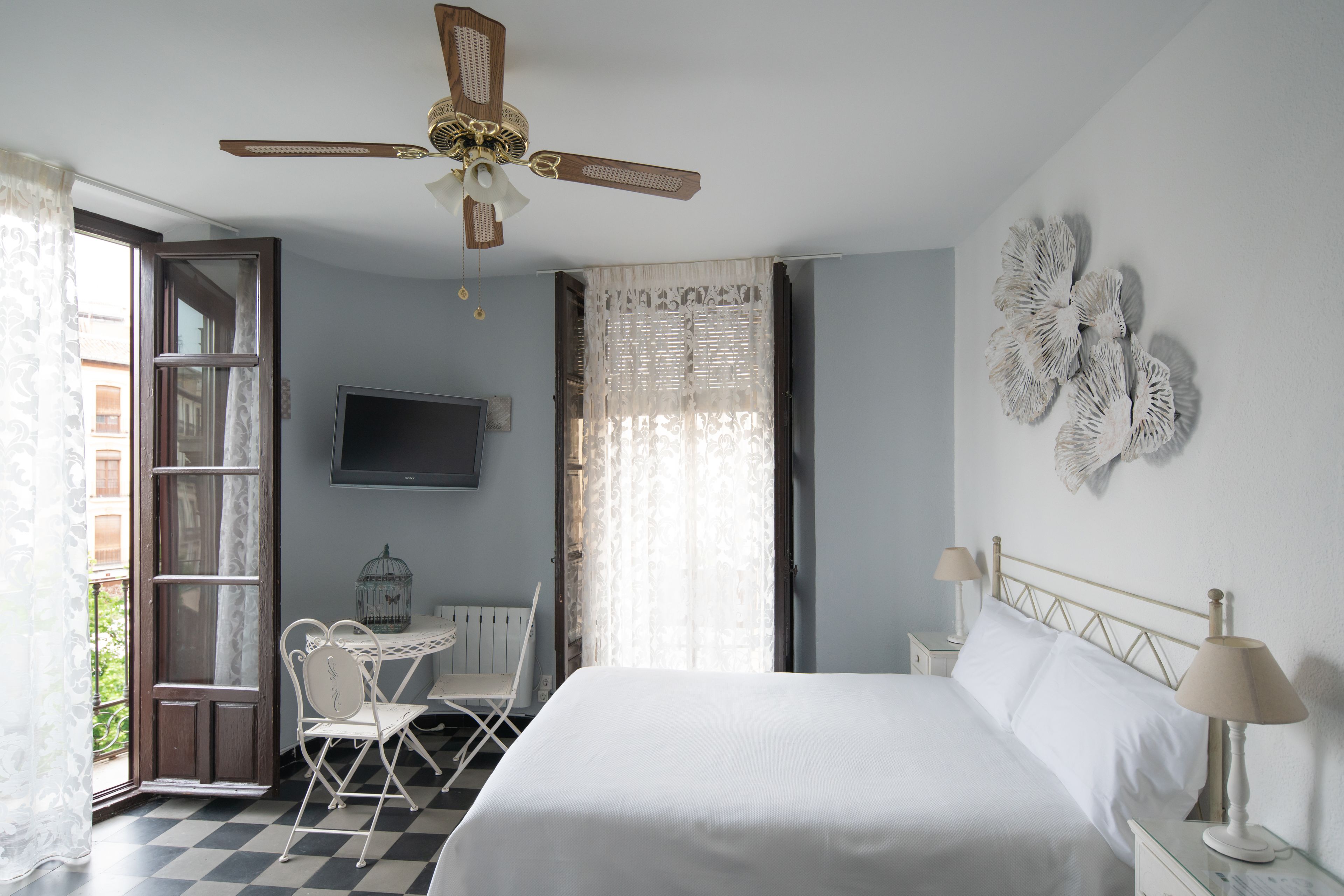 A hotel room with a bed, a desk, a chair, a TV, and a ceiling fan.