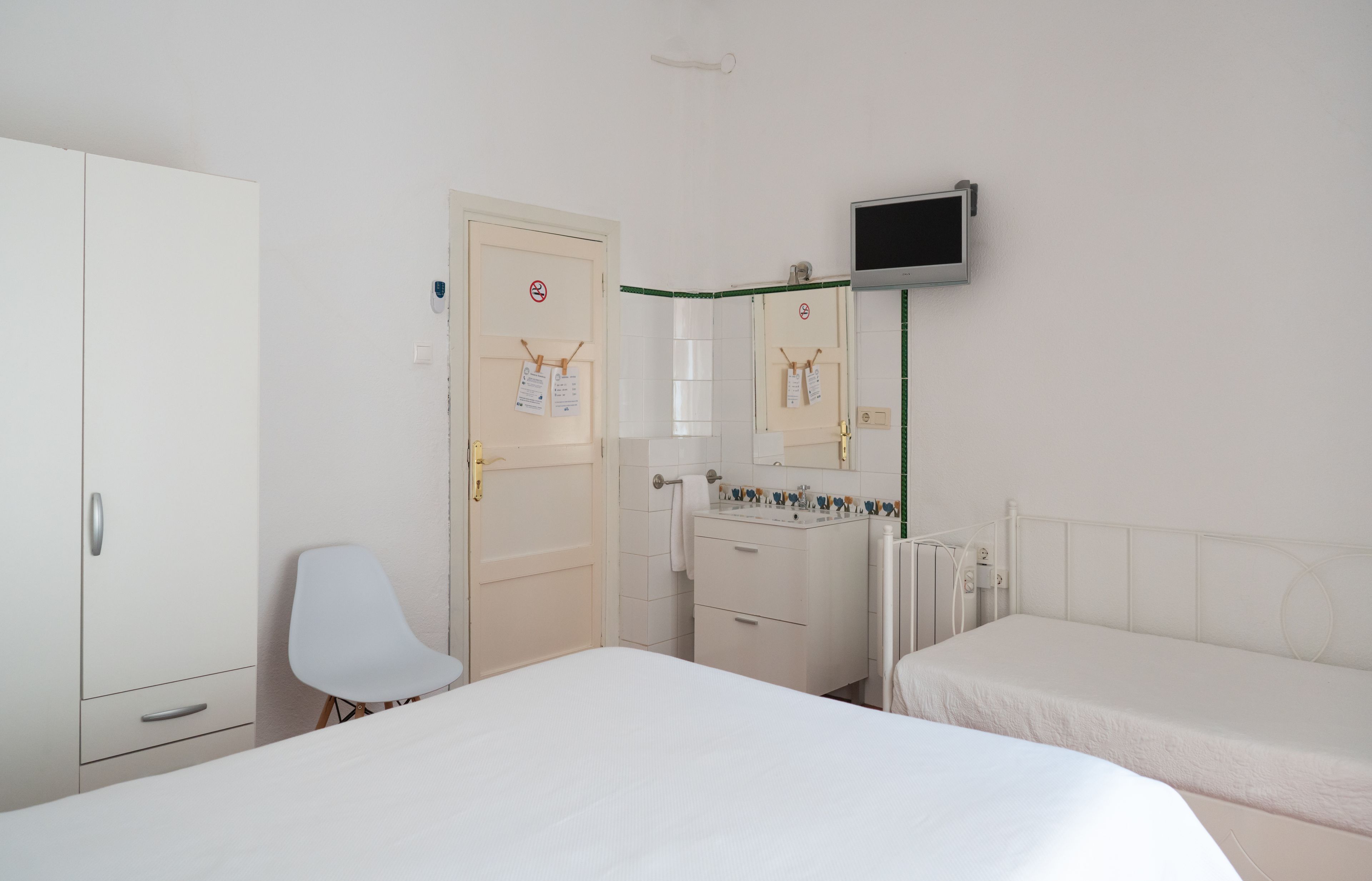 Een hotelkamer met twee bedden, een witte kast, een stoel, een bureau met een computer en een aan de muur bevestigde televisie.