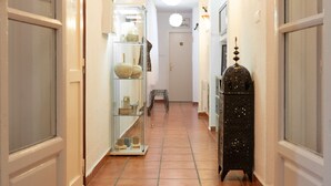 Un pasillo con suelo de baldosas, un expositor de vidrio, un taburete pequeño y un farol decorativo.