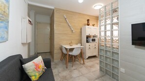 Un espacio habitable compacto con sofá, una pequeña mesa de comedor y un televisor montado en la pared.