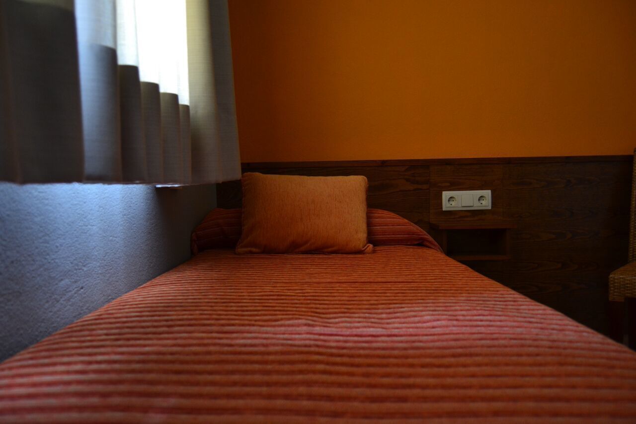 A single bed with a striped bedspread and a single pillow in a room with an orange wall and a wooden headboard.