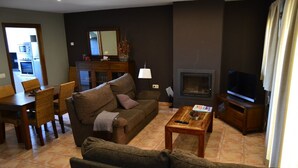 Un salon comprenant un canapé, une table basse, une cheminée, un téléviseur et un coin repas avec des chaises et une table.