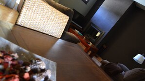 Un salon moderne avec un parquet en bois foncé, un canapé marron, une table basse en osier et une cheminée.