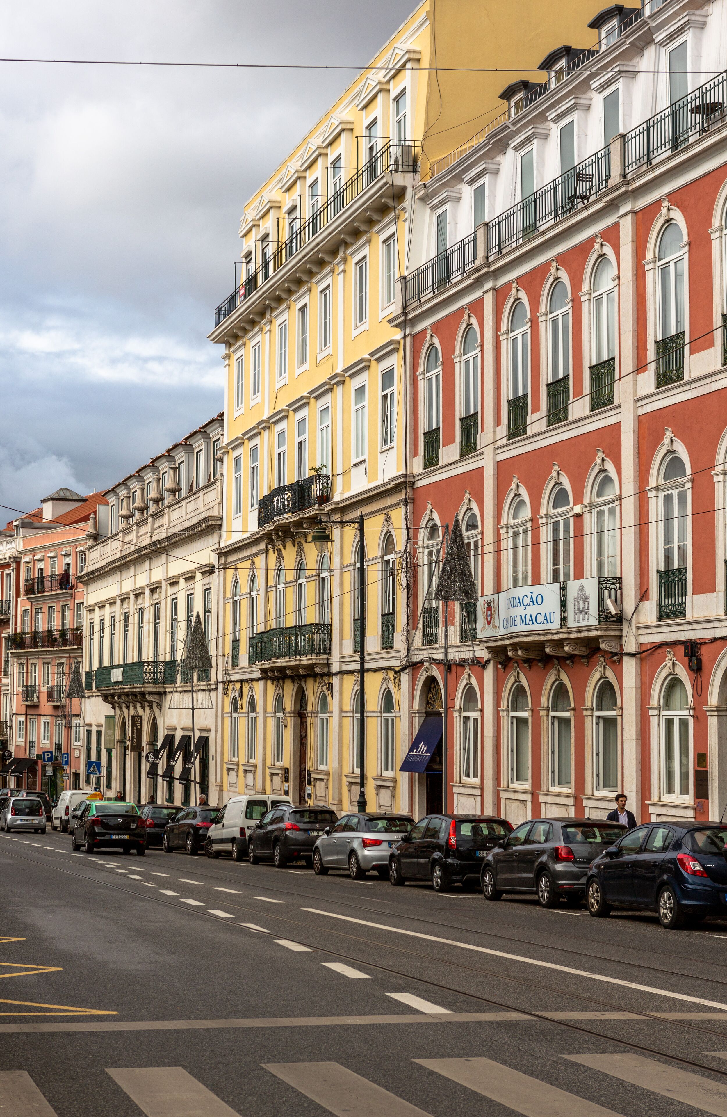 A row of colorful buildings with balconies, parked cars, and a clear sky.