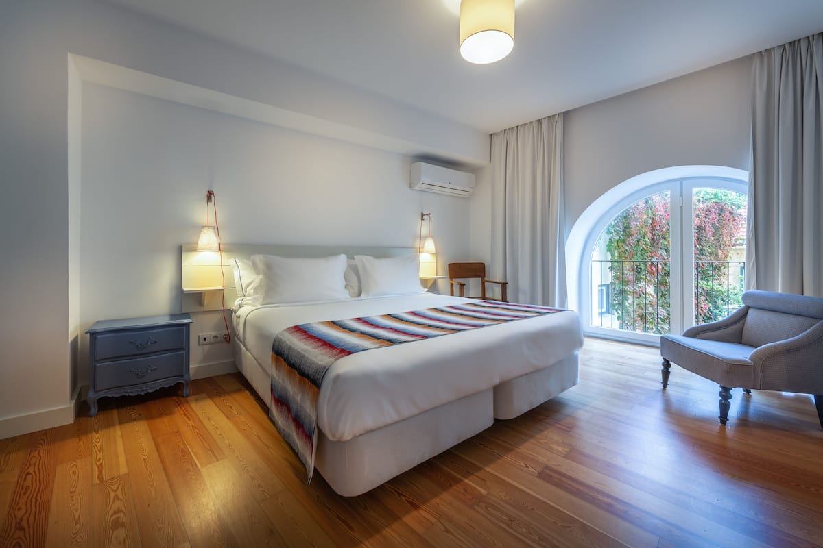 Un dormitorio con una cama grande, una mesita de noche, una silla y una ventana con cortinas.