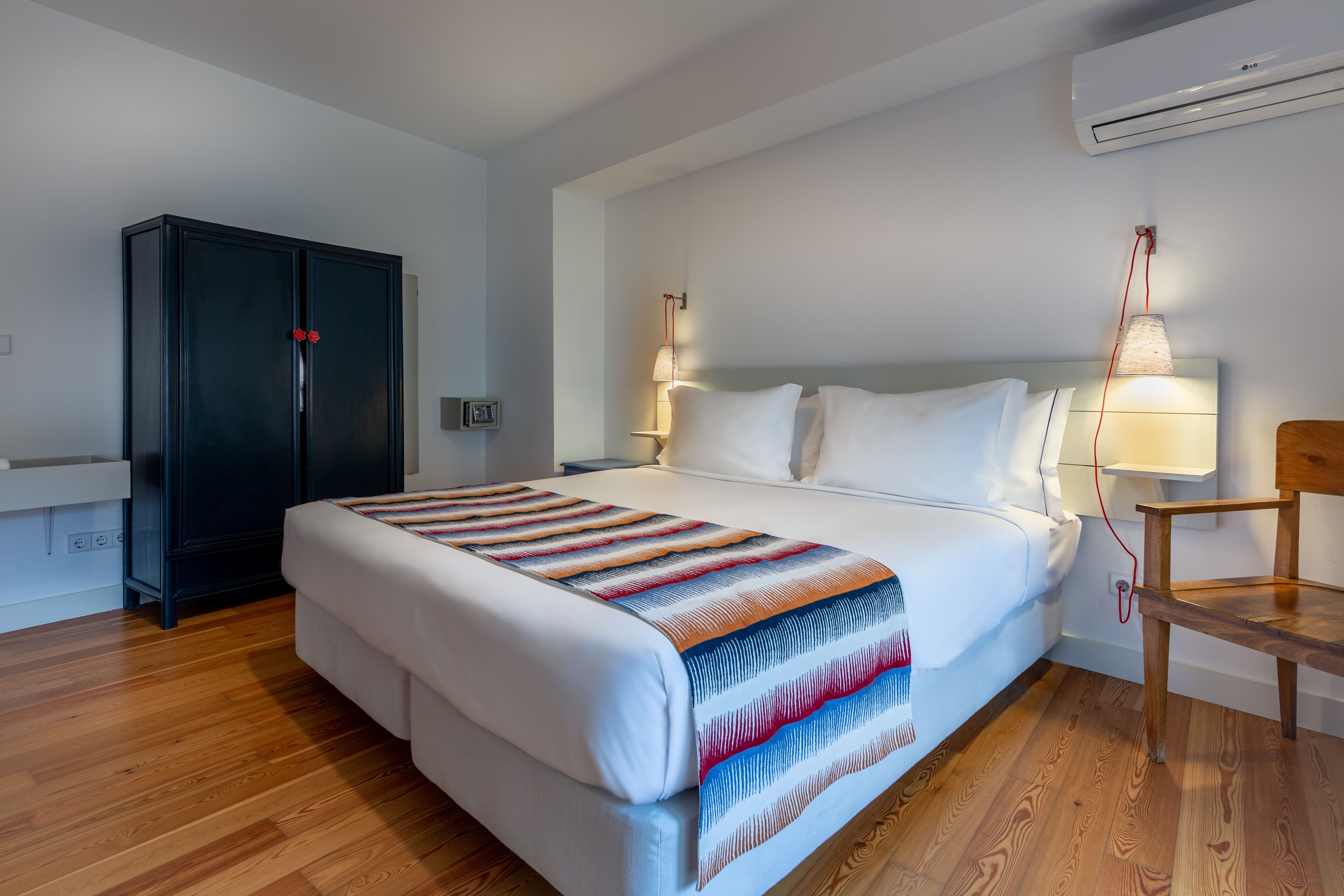 Quarto de hotel com uma cama grande, um guarda-roupa, uma secretária e uma cadeira.