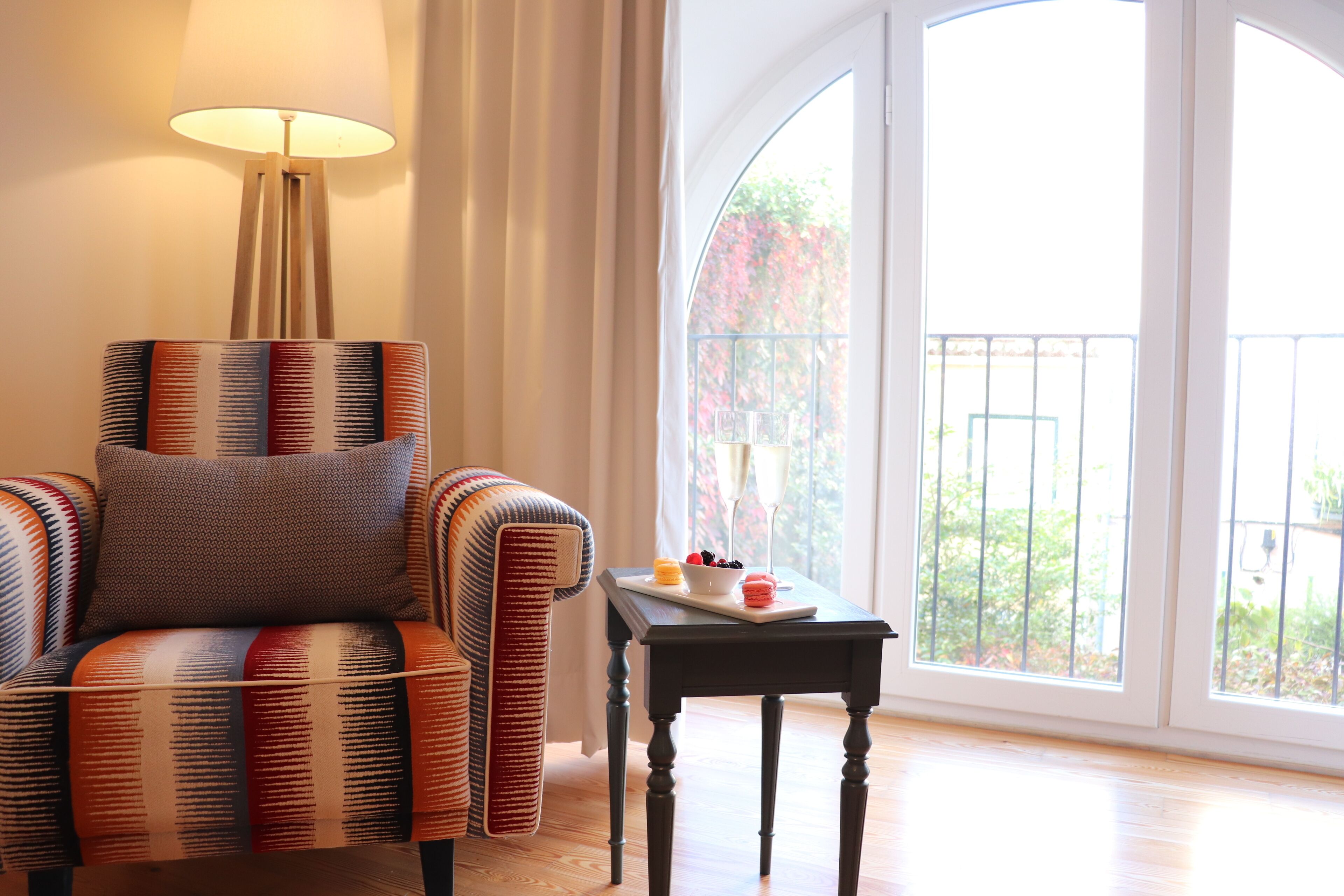 Quarto com uma poltrona estampada, uma pequena mesa com uma bandeja de comida e uma janela grande com vista para o verde.