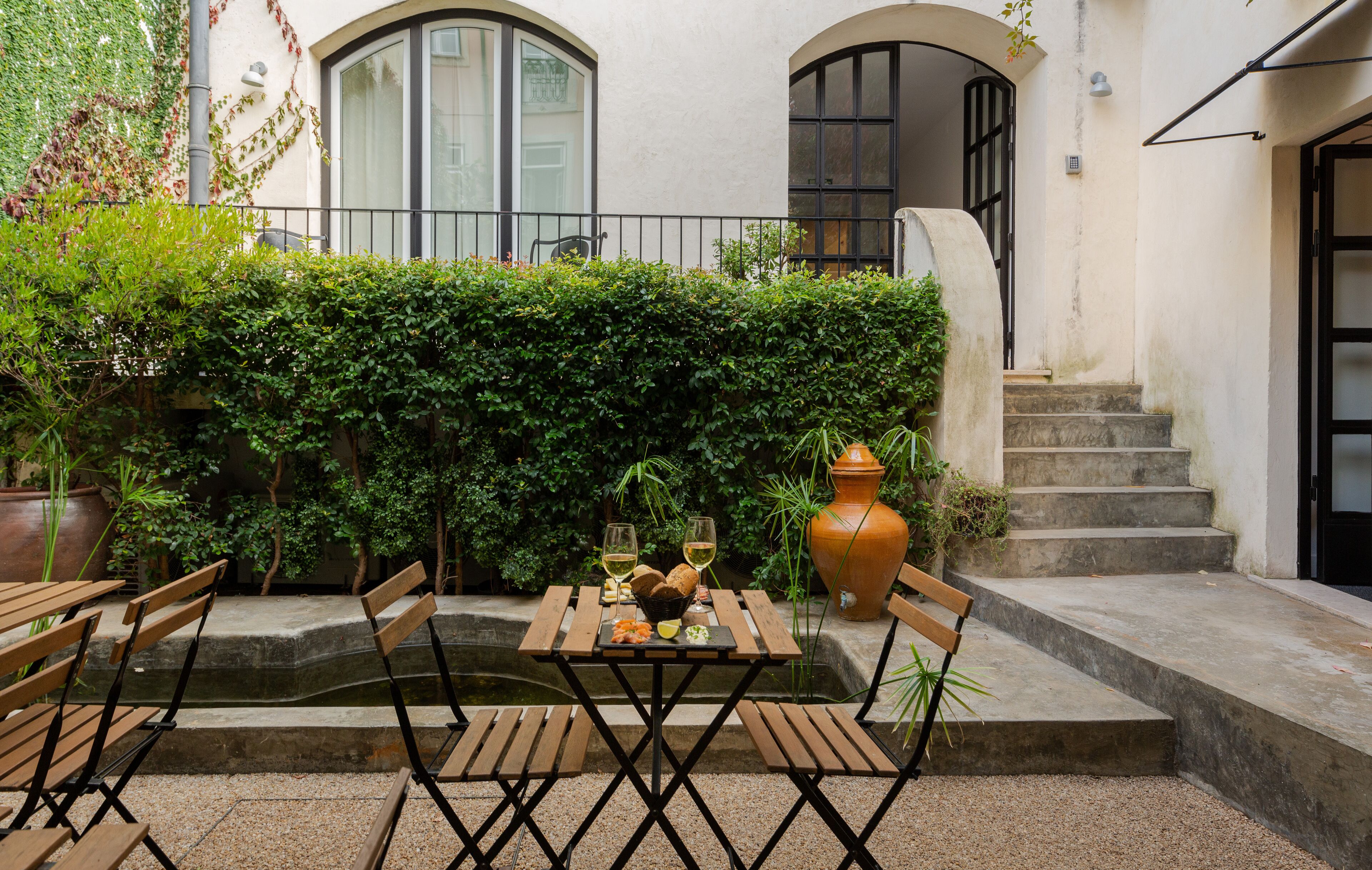 An outdoor patio with wooden tables and chairs, a small fountain, and a large terracotta pot.