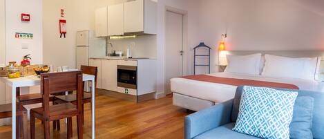 A compact hotel room with a kitchenette, a dining area, and a bed with a patterned pillow.