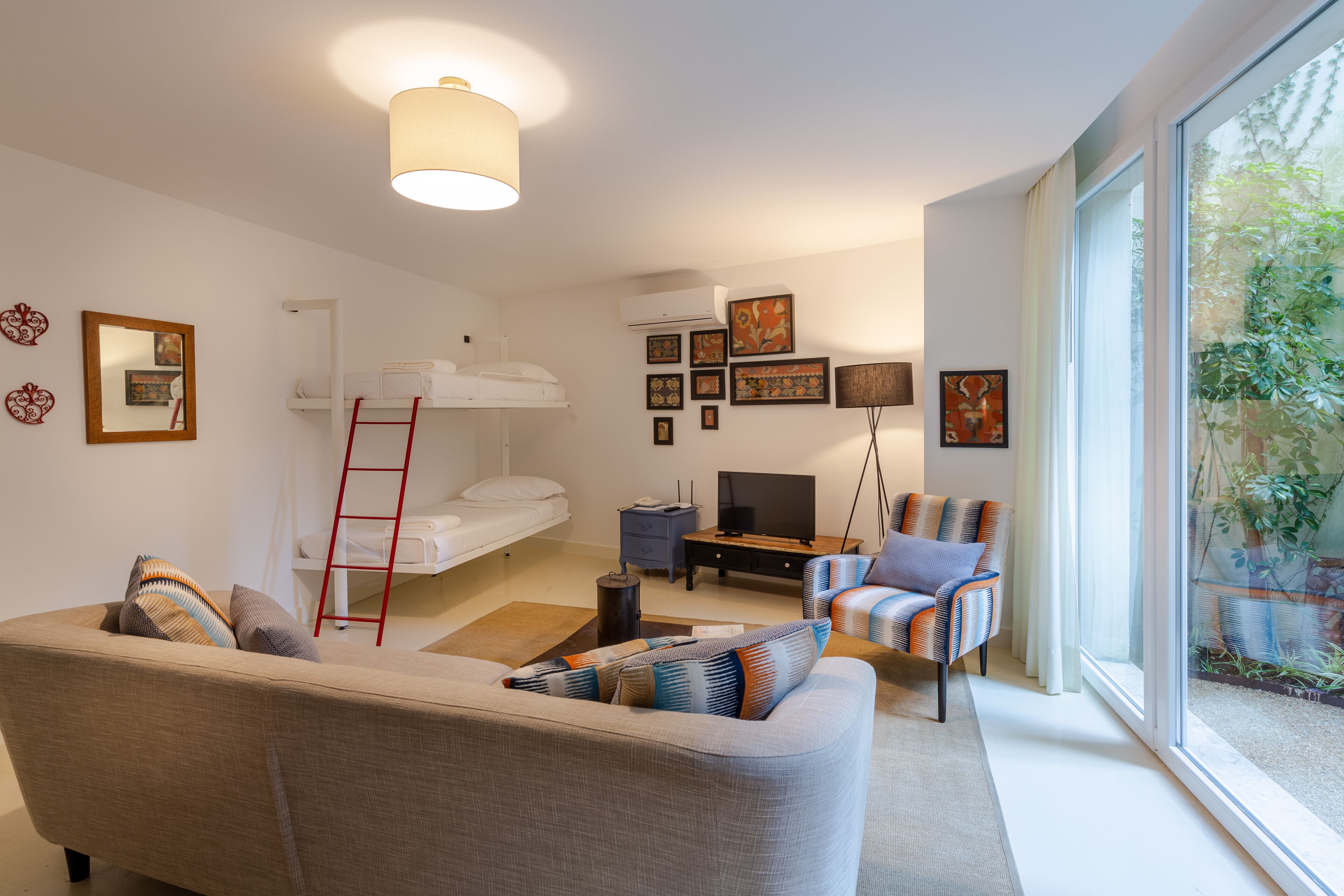 A modern living room with a sofa, a TV, a bunk bed, and a large window with a view of greenery.