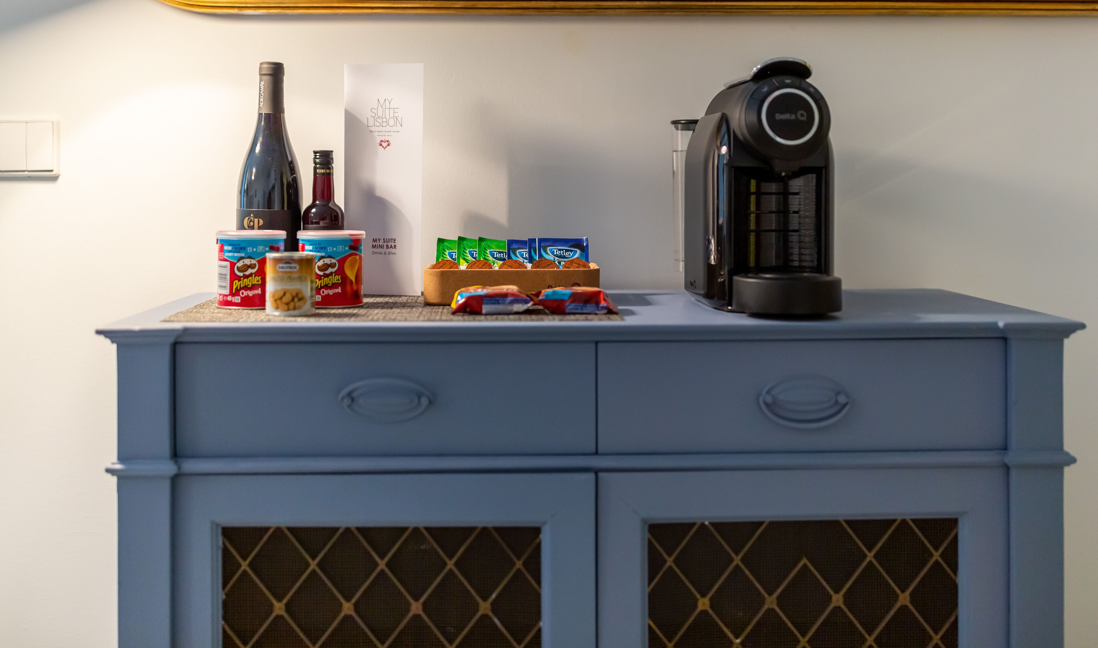 Eine Minibar mit einer Weinflasche, Pringles-Dosen, Tetley-Teebeuteln und einer Kaffeemaschine.