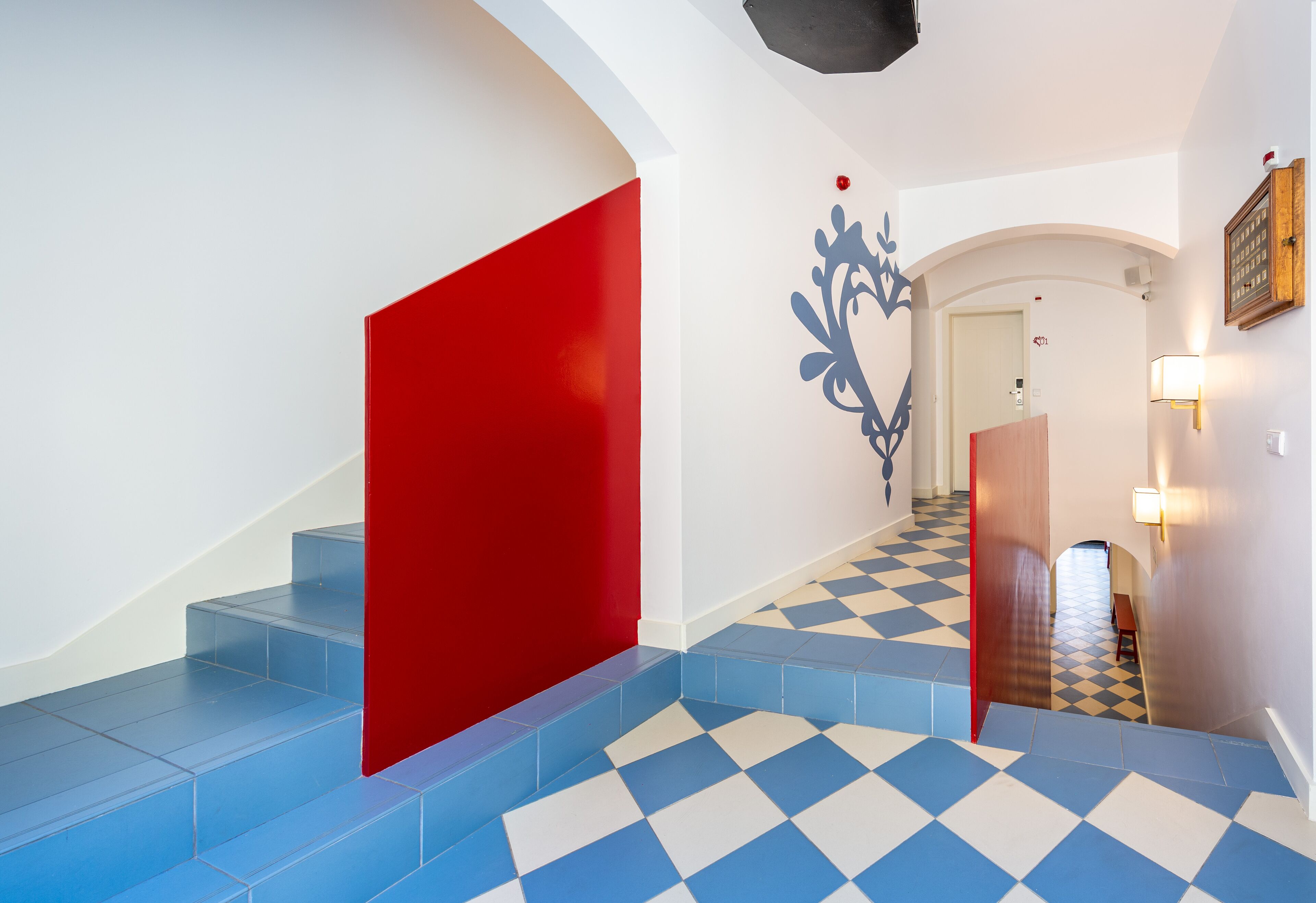 A staircase with blue and white checkered flooring, a red accent wall, and a decorative wall piece.