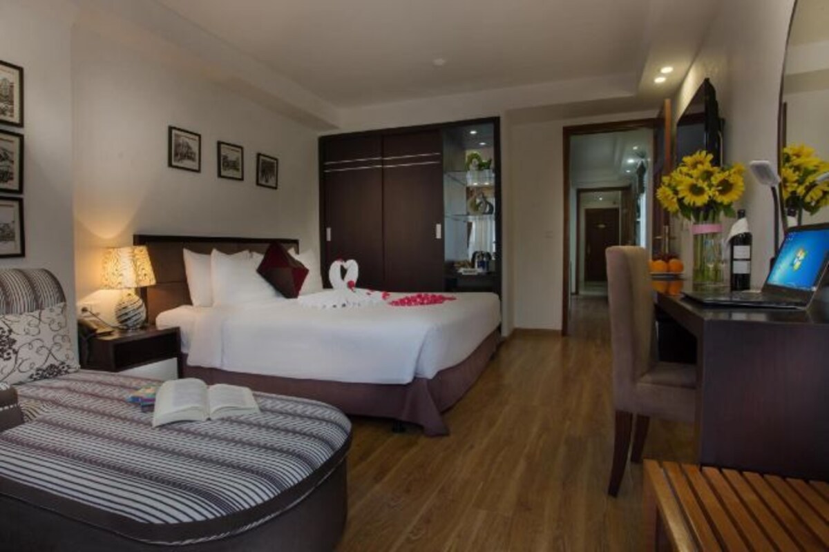 A hotel room with a bed, bedside table, lamp, and a desk with a laptop.