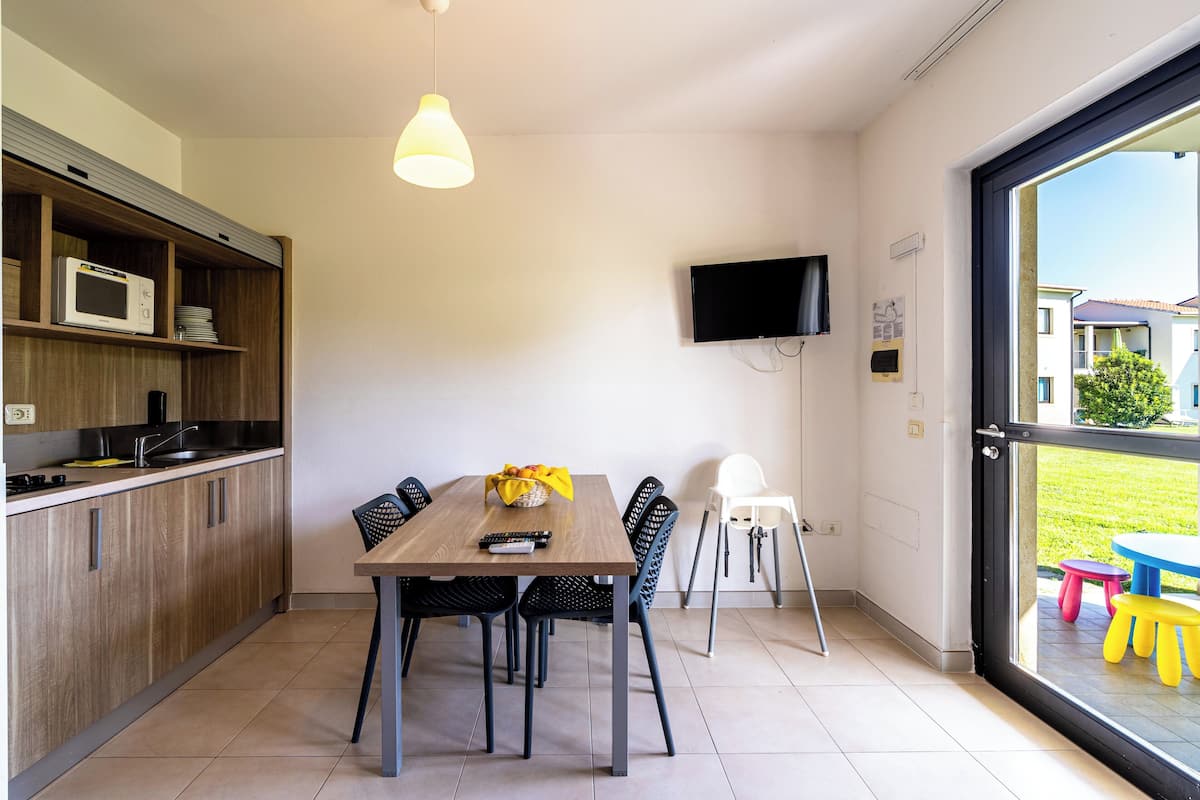 Een moderne keuken met een eettafel, stoelen, een aan de muur bevestigde televisie en uitzicht door een groot raam.