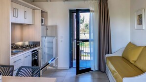 A compact kitchen with modern appliances, a dining area with a table and chairs, and a sofa with a yellow cushion. - Belvedere Village (Castelnuovo del Garda)