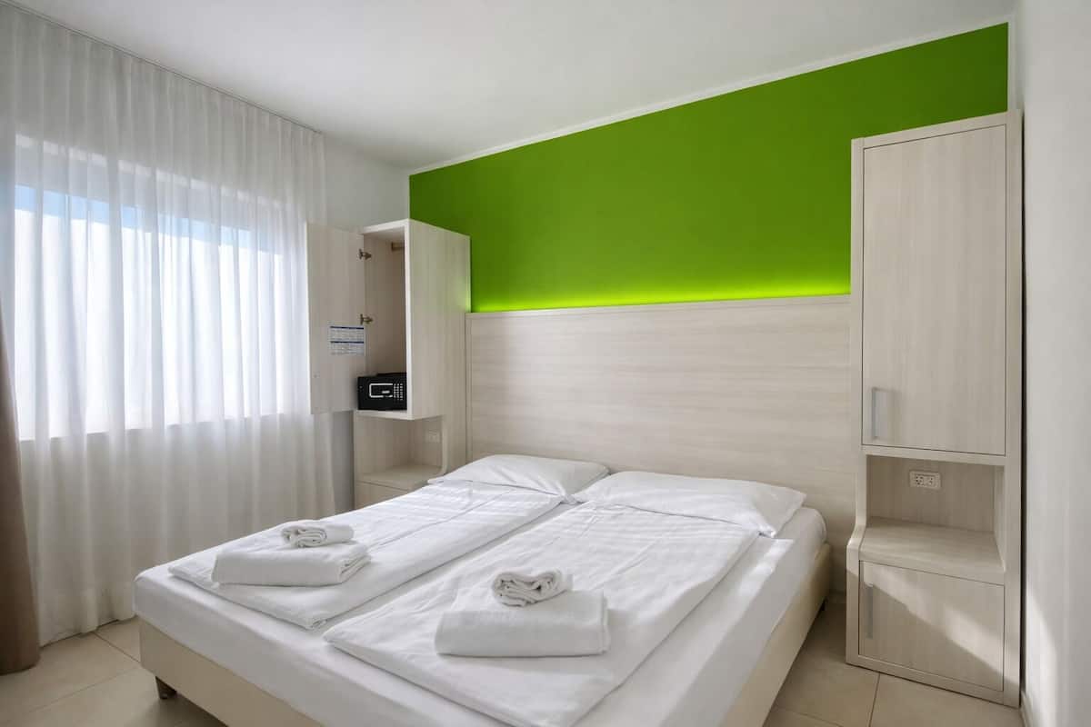 Een hotelkamer met een bed, nachtkastje, spiegel en een groene accentmuur.
