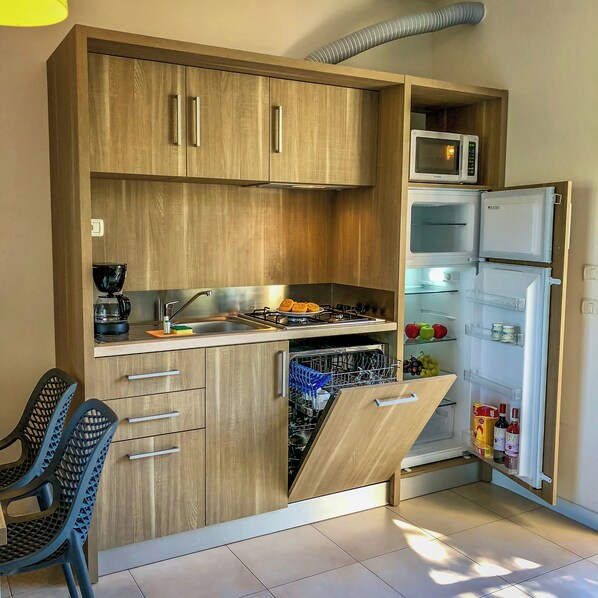 A compact kitchen with wooden cabinets, a built-in microwave, a dishwasher, and a refrigerator. - Belvedere Village (Castelnuovo del Garda)