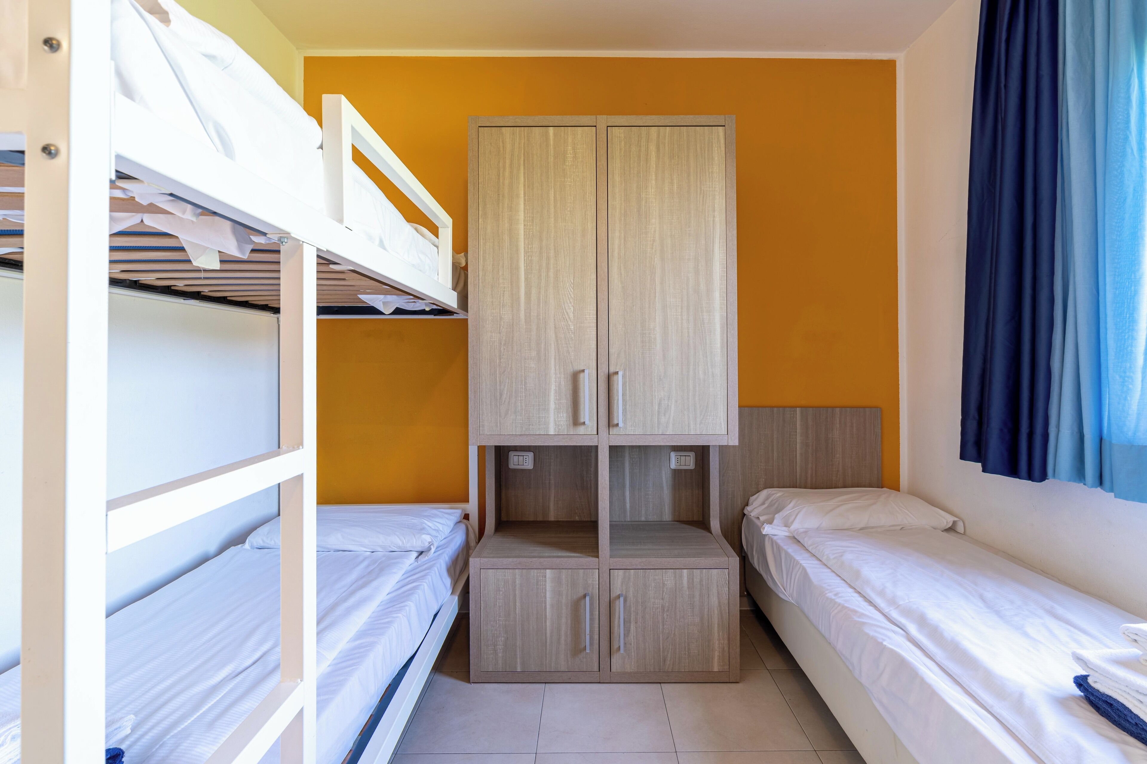 Un dormitorio con literas, un armario y una ventana con cortinas.