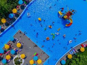 An aerial view of a swimming pool area with multiple lanes, sun loungers, and umbrellas. - Belvedere Village (Castelnuovo del Garda)