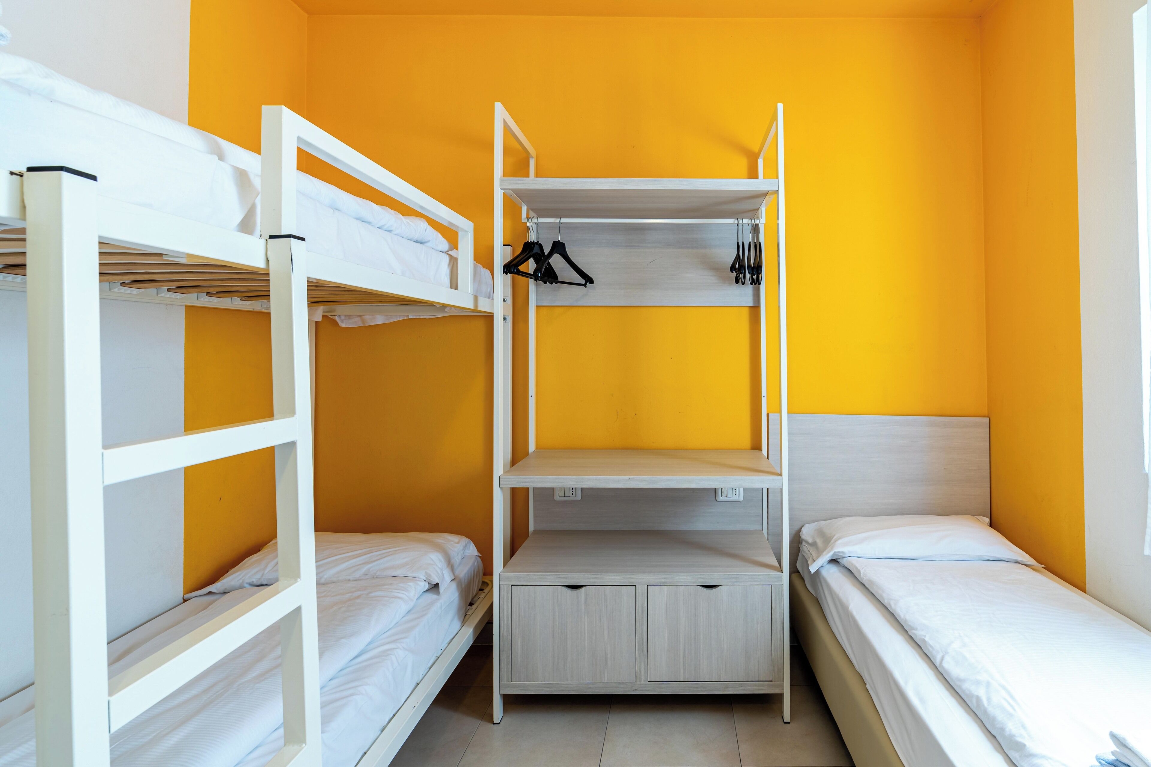 A dormitory room with bunk beds, a central shelf unit, and a single bed.