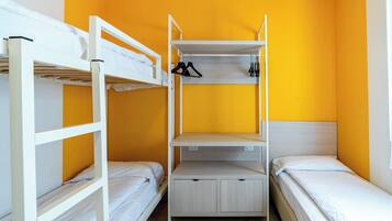 A dormitory room with bunk beds, a central shelf unit, and a single bed.