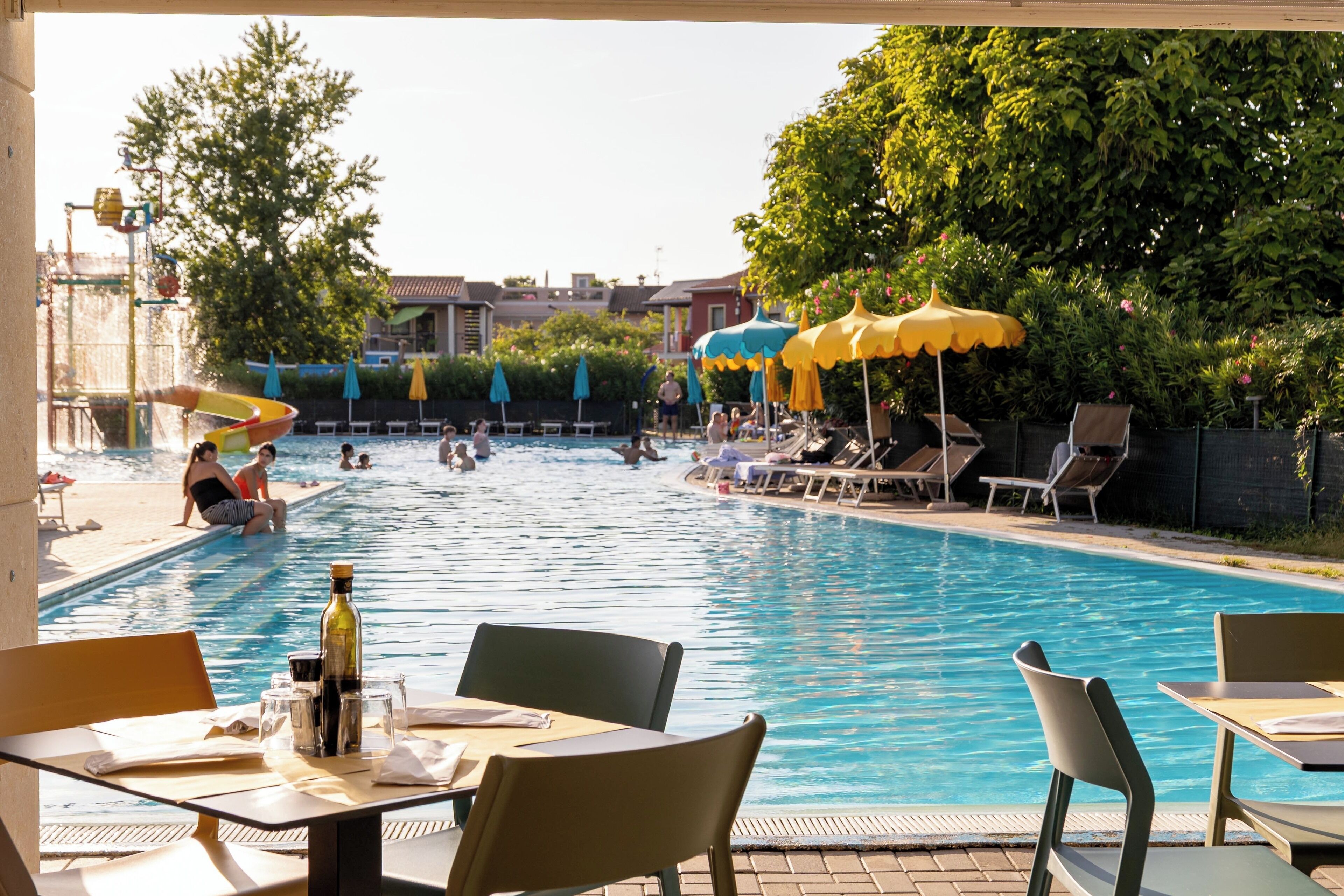 A pool area with lounge chairs, umbrellas, and a dining table with chairs.